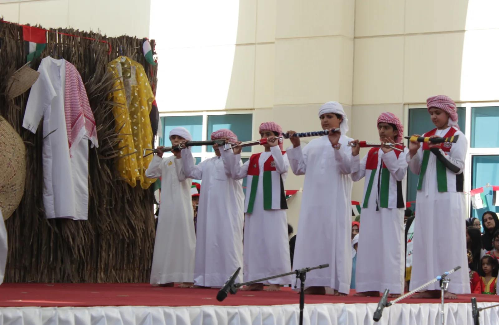 Emirati boys in white traditional dress performing Al-Ayyala (Yowlah) at a UAE National Day celebration, holding rifles in the characteristic two-row formation of the traditional performing art inscribed on UNESCO's Representative List as File 01012 (9.COM, 2014, UAE and Oman)