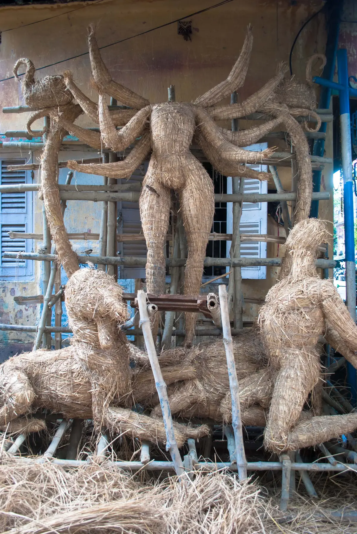 Straw and bamboo armature of a Durga Puja idol under construction at Kumortuli, Kolkata — showing the 10-armed goddess and flanking deities in the initial construction stage. Kumortuli artisans build these clay idols over months before the festival
