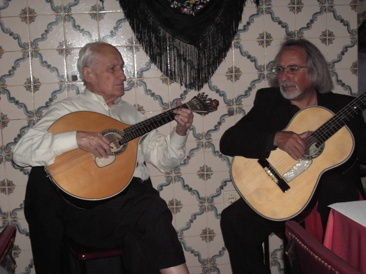 Two musicians at a fado restaurant in Lisbon playing the guitarra portuguesa (pear-shaped 12-string cittern) and viola baixo — the two defining instruments of the fado tradition inscribed by UNESCO in 2011