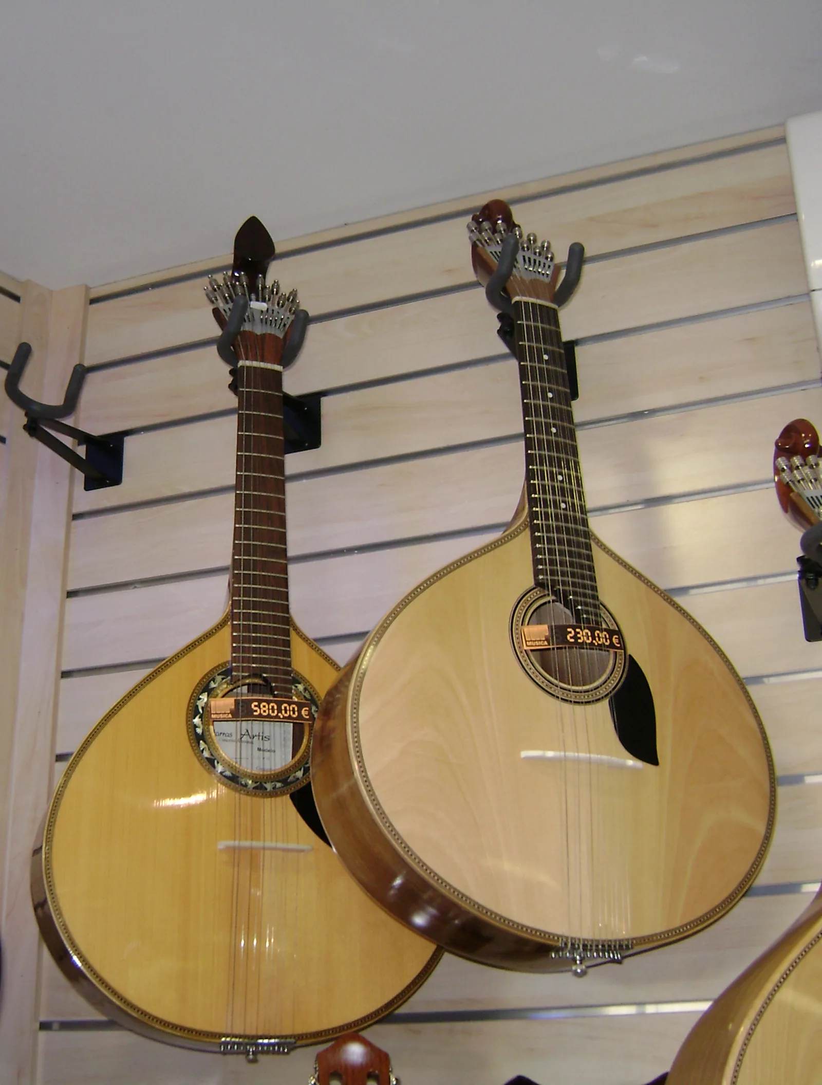 Two Portuguese guitarra instruments side by side — the Coimbra variant (left, longer neck) and the Lisbon variant (right, rounder body) — illustrating the distinct regional constructions of the pear-shaped 12-string cittern that is the defining instrumental voice of fado under UNESCO's inscription File 00563
