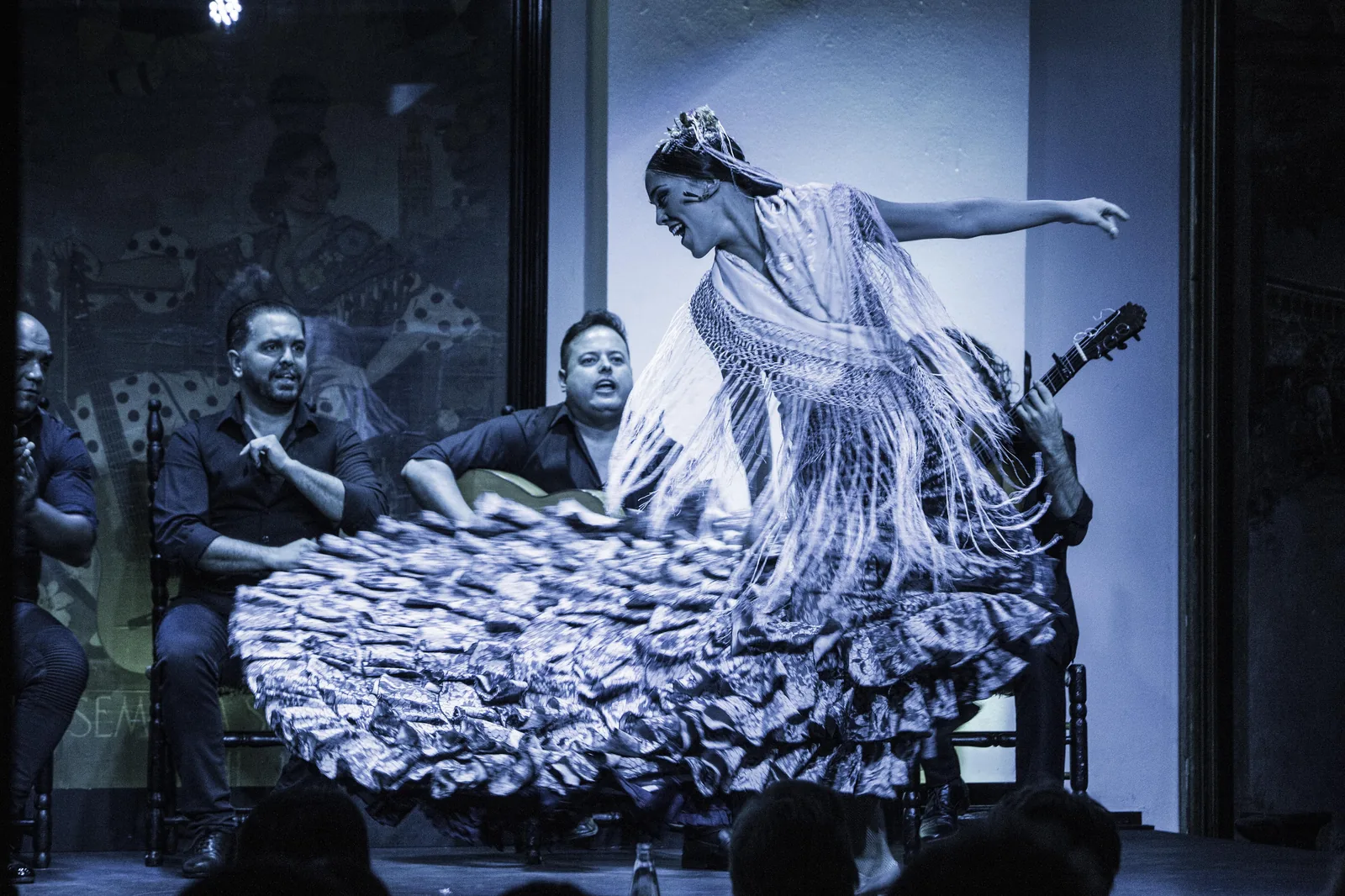 Flamenco performance at Tablao Flamenco El Arenal in Seville, Spain — bailaora in white fringed dress dancing alongside guitarists and cantaores, showing the cante (song), baile (dance), and toque (guitar) elements inscribed on UNESCO's Representative List as intangible cultural heritage File 00363