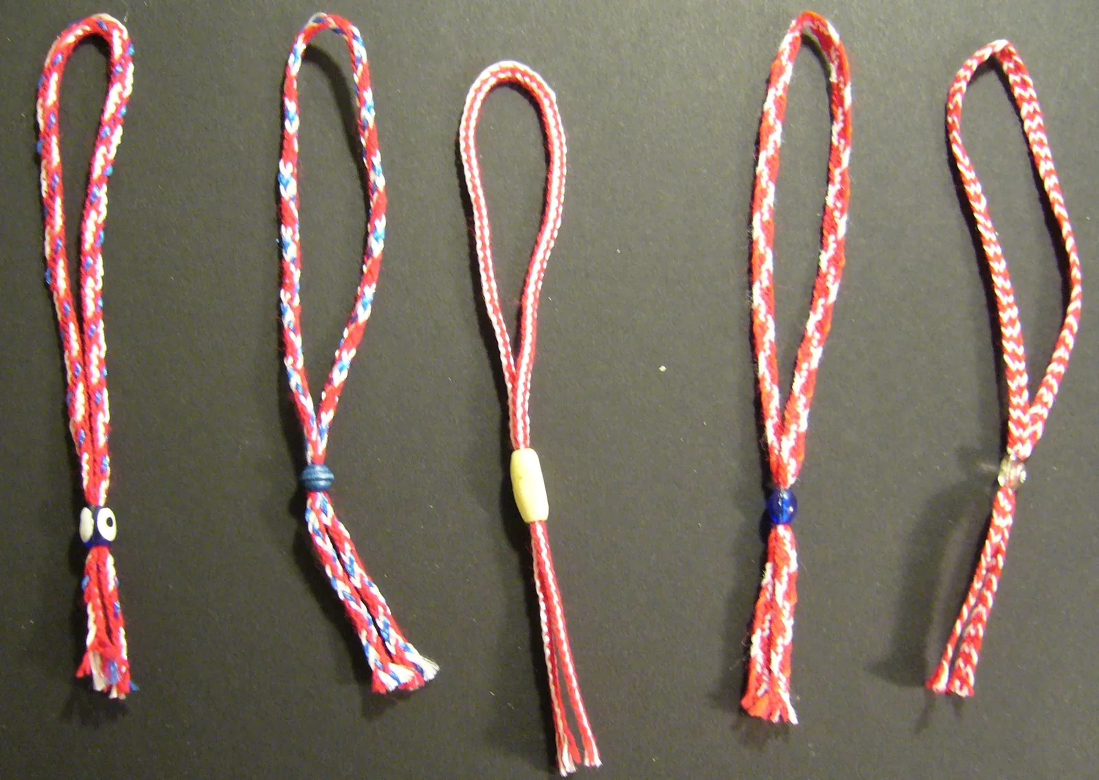 Five Martenitsa bracelets in braided red and white thread patterns with beads and tassels Bulgarian spring tradition — Cultural practices associated to 1st of March UNESCO Representative List Intangible Cultural Heritage 2017