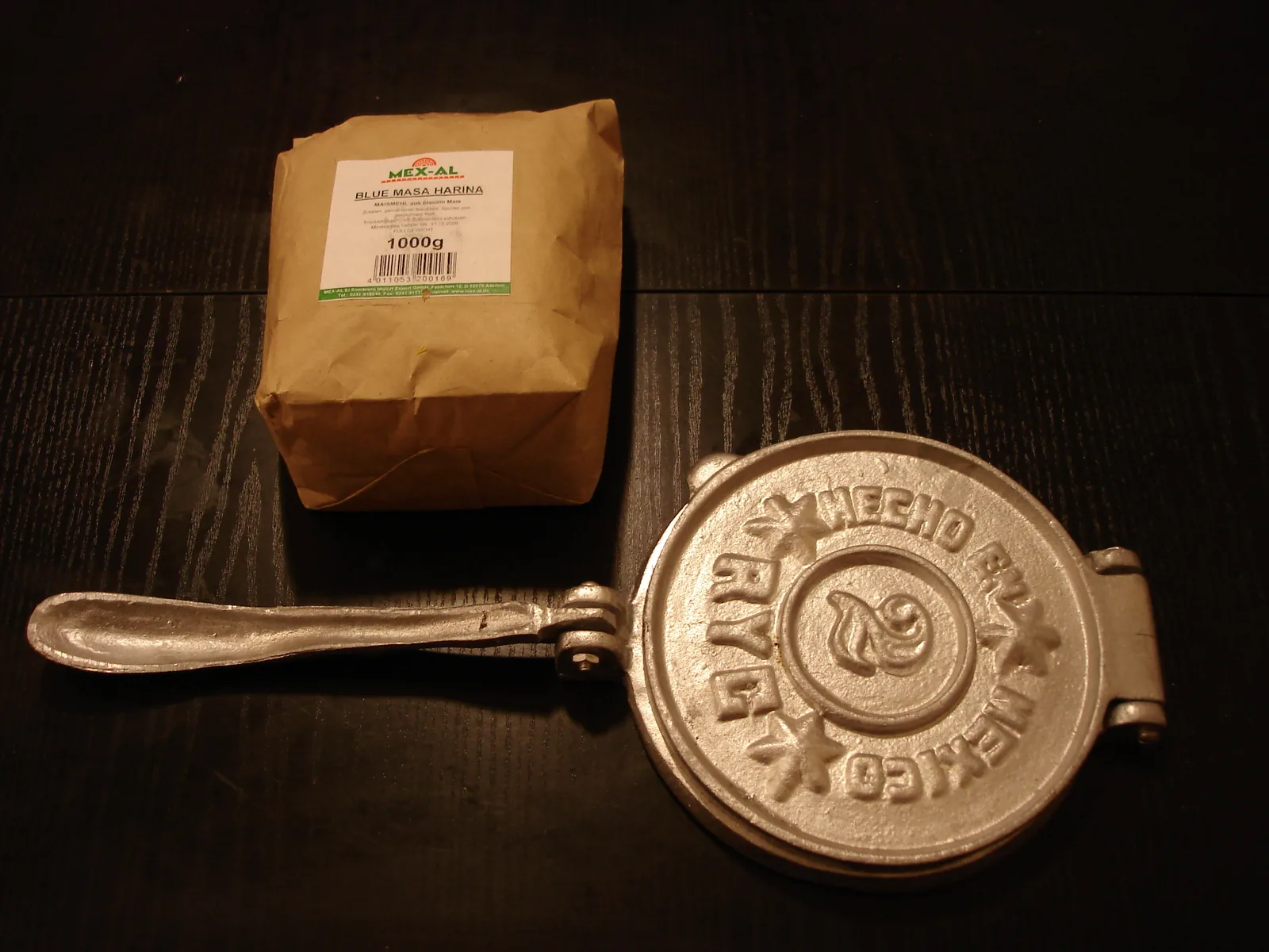 Traditional cast-iron tortilla press and masa harina — the tools of traditional Mexican tortilla-making, the craft at the heart of the Traditional Mexican cuisine UNESCO inscription (File 00400, 2010, Michoacán paradigm), which recognizes corn processing through nixtamalization and the milpa agricultural system as living intangible cultural heritage