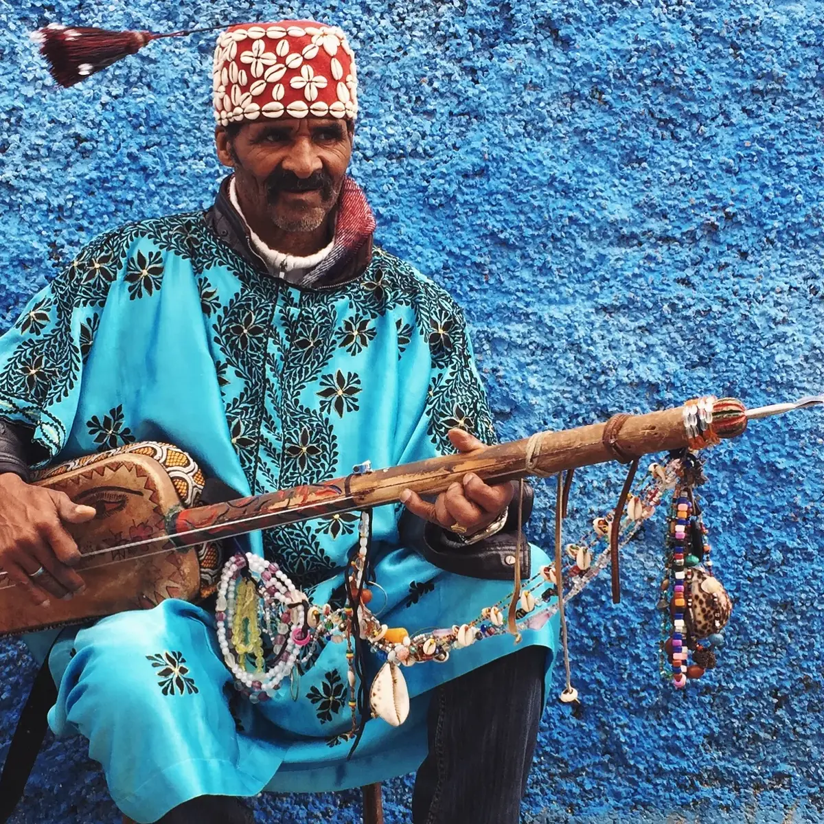 Gnawa musician in traditional blue djellaba playing a sintir lute — Gnaoua music is among the living cultural practices recognized at Jemaa el-Fna by UNESCO