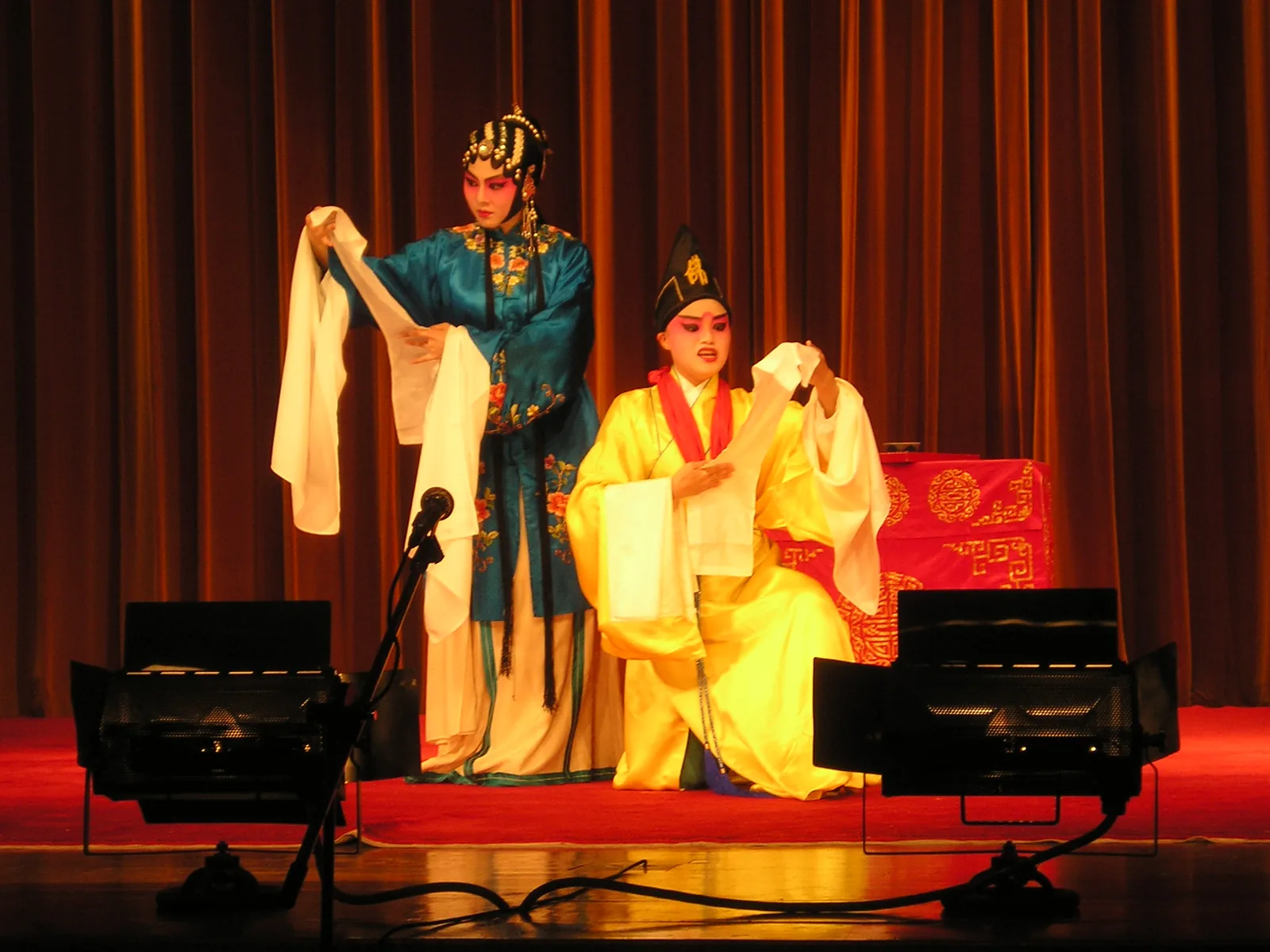 Two Kunqu opera performers on stage in embroidered Ming-dynasty costumes with characteristic water-sleeve gestures — Kunqu originated in Kunshan, Suzhou in the 14th century and reached its classical form through Wei Liangfu's Ming-dynasty reforms, with The Peony Pavilion (1598) as its most celebrated work