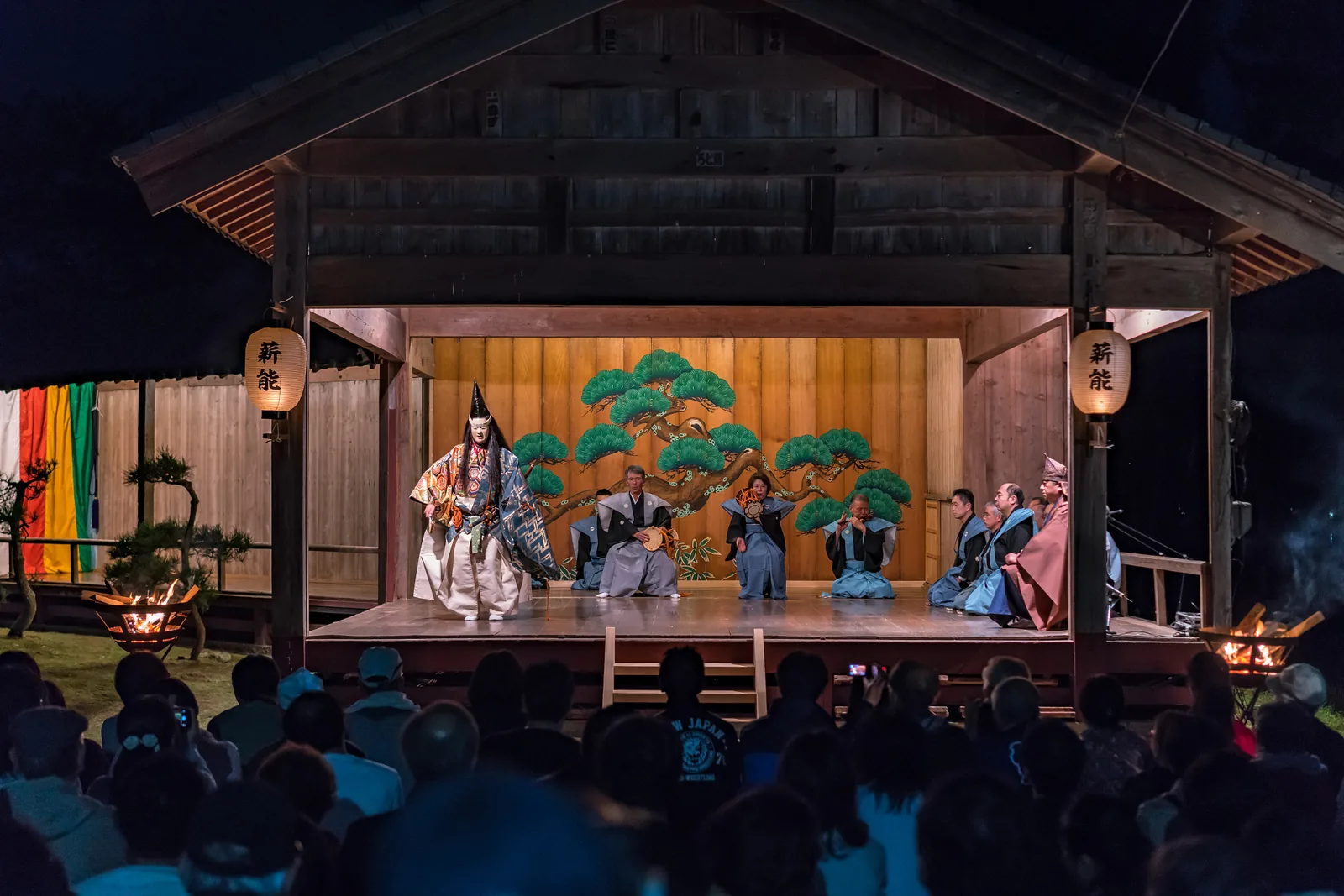 Noh theatre performance at night on Sado Island Japan with masked shite actor in elaborate costume before painted pine backdrop and seated musicians — Nogaku theatre (File 00012, Japan, 2008) is one of the founding inscriptions on UNESCO's Representative List of the Intangible Cultural Heritage of Humanity