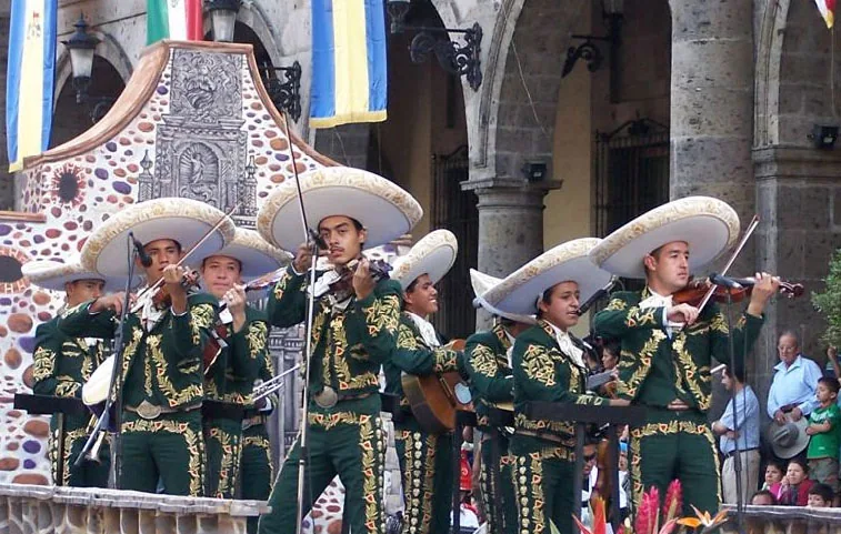 Mariachi ensemble in green charro costumes with wide-brimmed sombreros performing at the XIII Encuentro Internacional del Mariachi y la Charreria in Guadalajara, Jalisco — the International Mariachi Festival in Guadalajara, with colonial architecture in the background, representing the tradition's deep roots in Jalisco recognized in UNESCO's 2011 ICH inscription