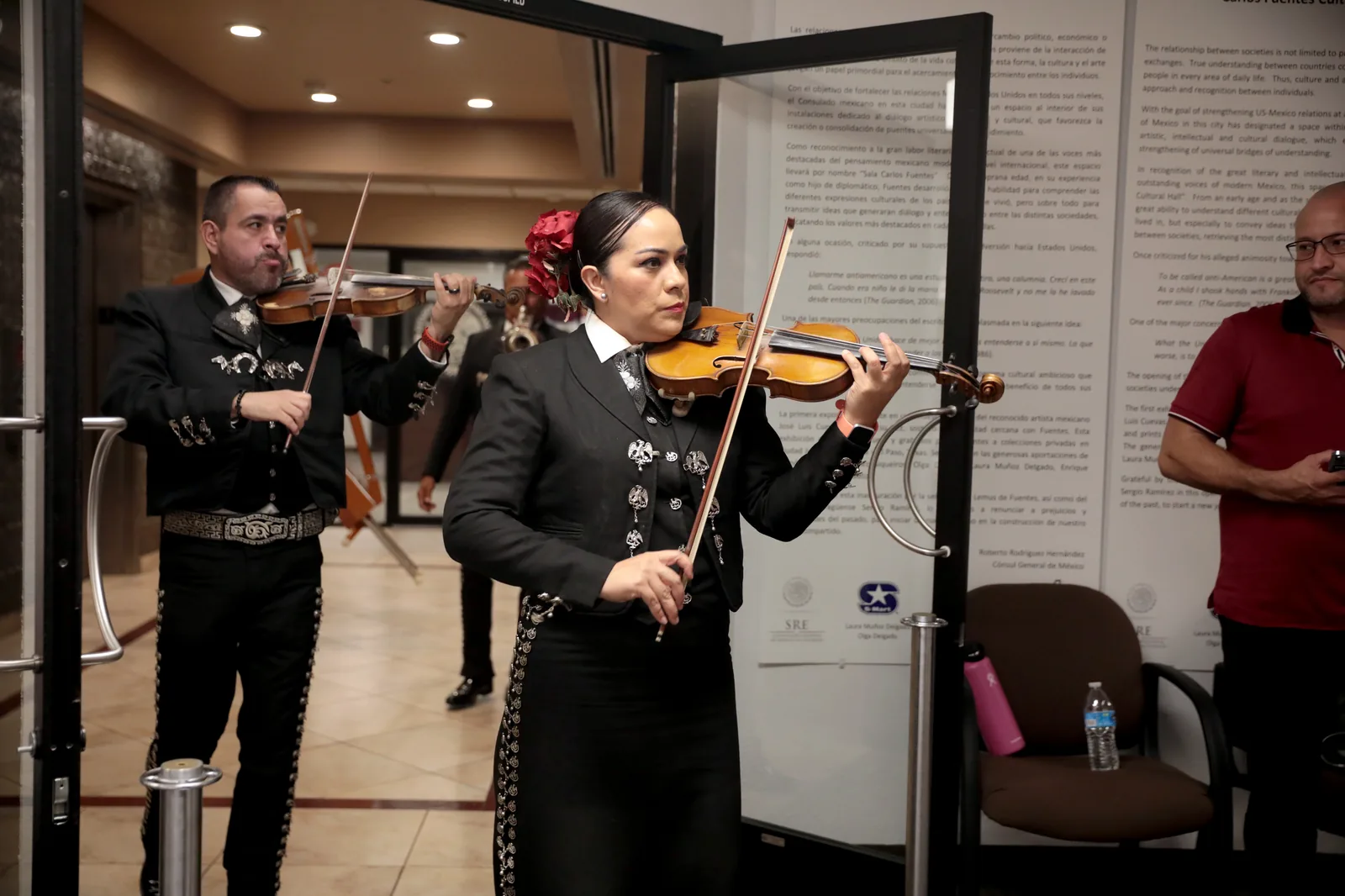 Female and male mariachi musicians in traditional black charro costume with silver embroidery playing violin at the Consulate General of Mexico in Phoenix (2022) — mariachi was inscribed on UNESCO's Representative List as intangible cultural heritage File 00575 in 2011