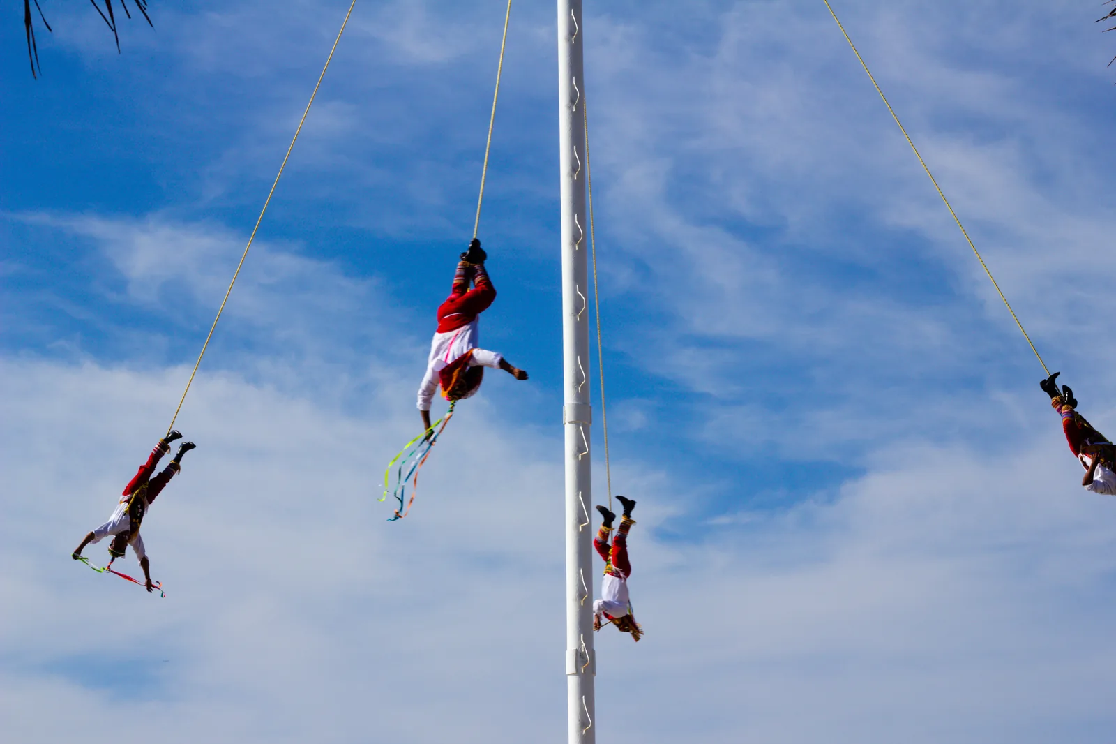 Four Totonac Voladores in traditional red and white costume descending on ropes from the pole against a blue sky in Puerto Vallarta, Mexico — the Ritual Ceremony of the Voladores (File 00175) was inscribed on UNESCO's Representative List as Mexico's intangible cultural heritage in 2009