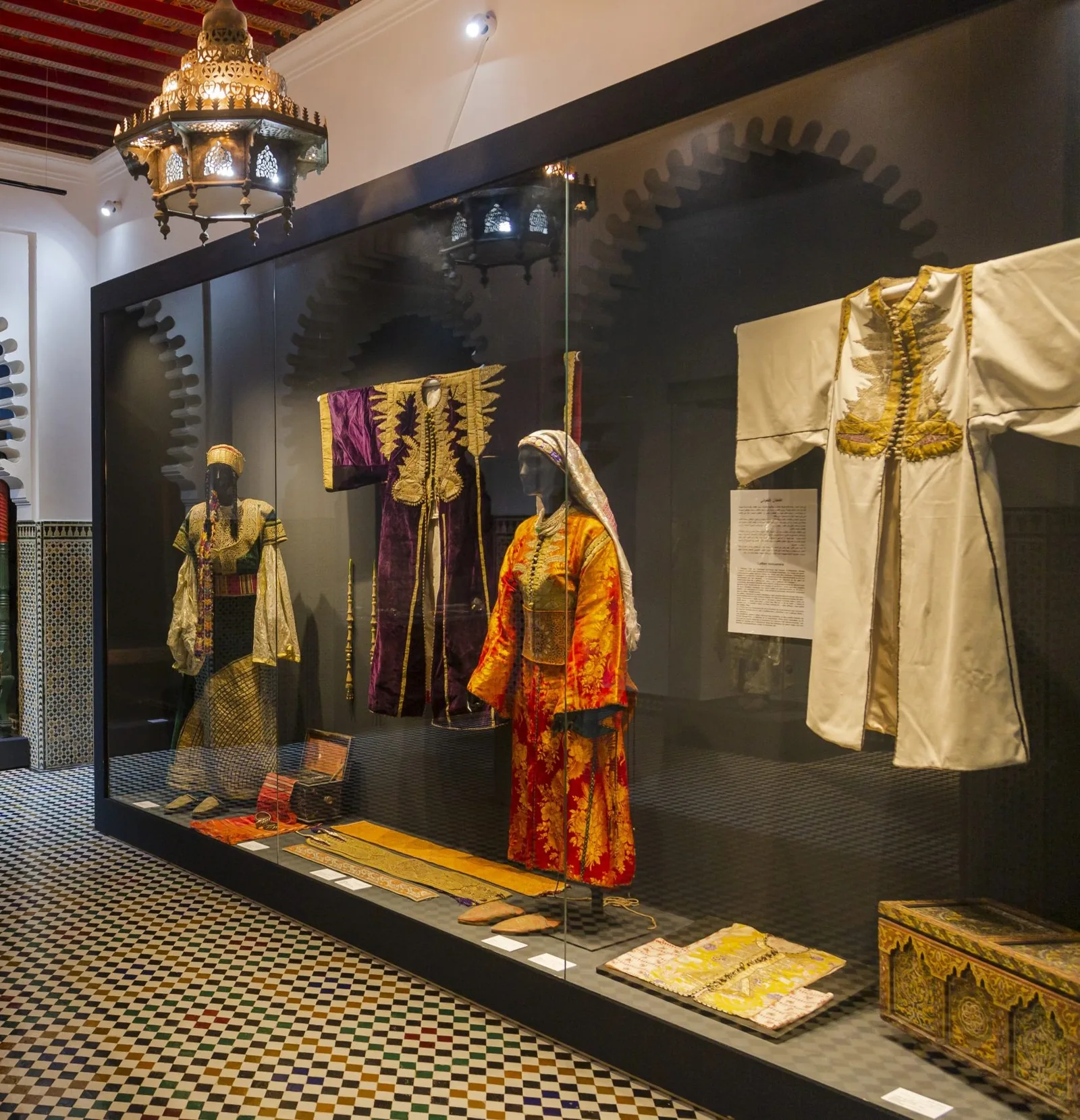 19th-century Moroccan caftans at the Bab El Oqla Museum in Tetouan showing historic examples of Tetouan's taajira embroidery tradition — the purple velvet caftan, brocade caftan on mannequin, and cream caftan represent regional variations of the artisanship tradition inscribed as UNESCO Intangible Cultural Heritage File 02077