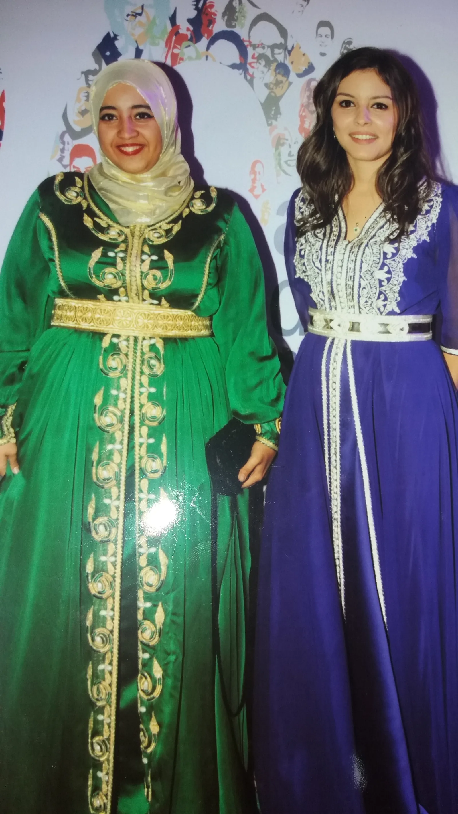 Two Moroccan women wearing traditional caftans at a celebration — the green silk caftan with elaborate gold sfifa and embroidered panels and the blue caftan with white decorative edge bands illustrate the ceremonial social role of the Moroccan caftan at weddings, religious holidays, and festive events, as documented in UNESCO ICH File 02077
