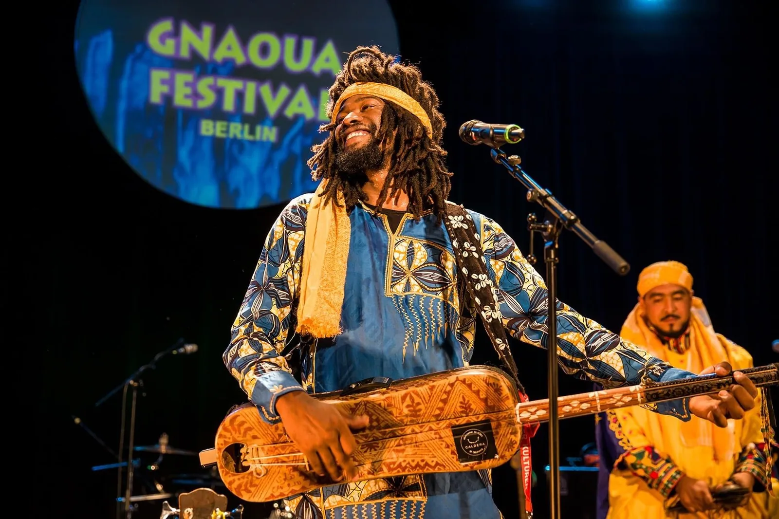 Gnawa maalem Mehdi Qamoum playing the guembri — the three-string bass lute central to the Gnawa lila ceremony — at the Gnaoua Festival Berlin 2019, demonstrating the international reach of Morocco's UNESCO-inscribed Gnawa tradition (File 01170, 2019) rooted in communities descended from enslaved sub-Saharan Africans