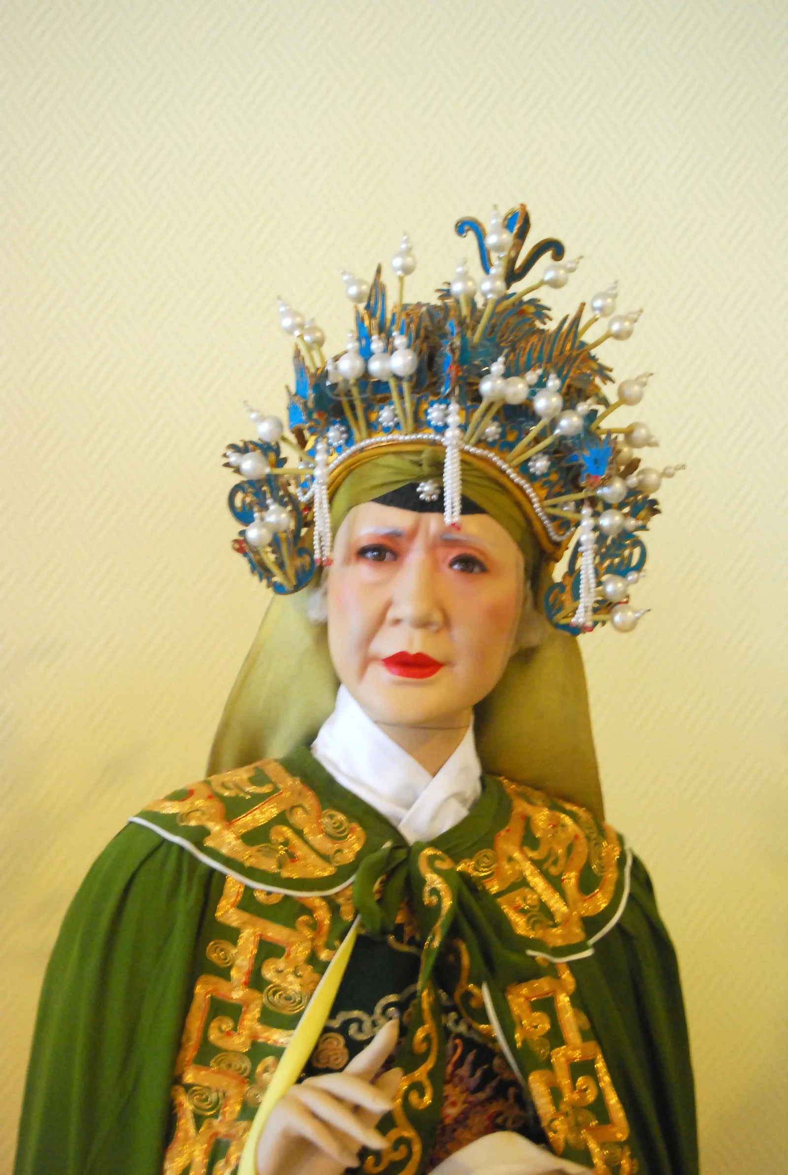 She Taijun (matriarch of the Yang Family Generals) in Lao Dan (elderly female) role — elaborate embroidered green military robe with pearl-studded headdress representing the traditional Dan role type in Peking opera that emerged in Beijing after the Four Anhui Troupes arrived in 1790 for Emperor Qianlong's birthday