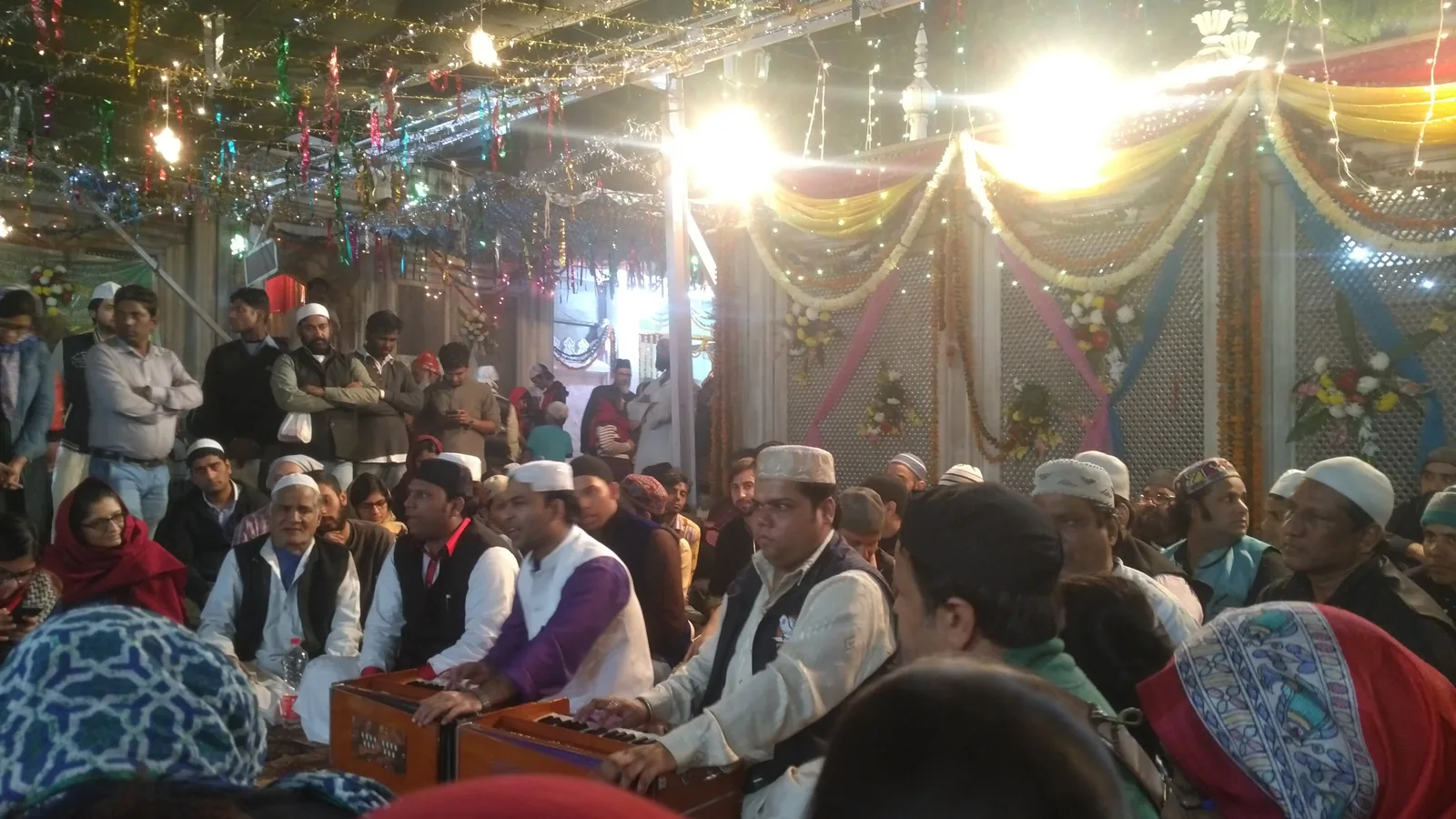 Qawwali ensemble performing with harmonium at the mehfil-e-sama at Hazrat Nizamuddin Dargah, Delhi — the shrine where Amir Khusrow served as disciple of Nizamuddin Auliya and where the Thursday-night qawwali gatherings that became the model for South Asian dargah performance were institutionalized in the 13th century