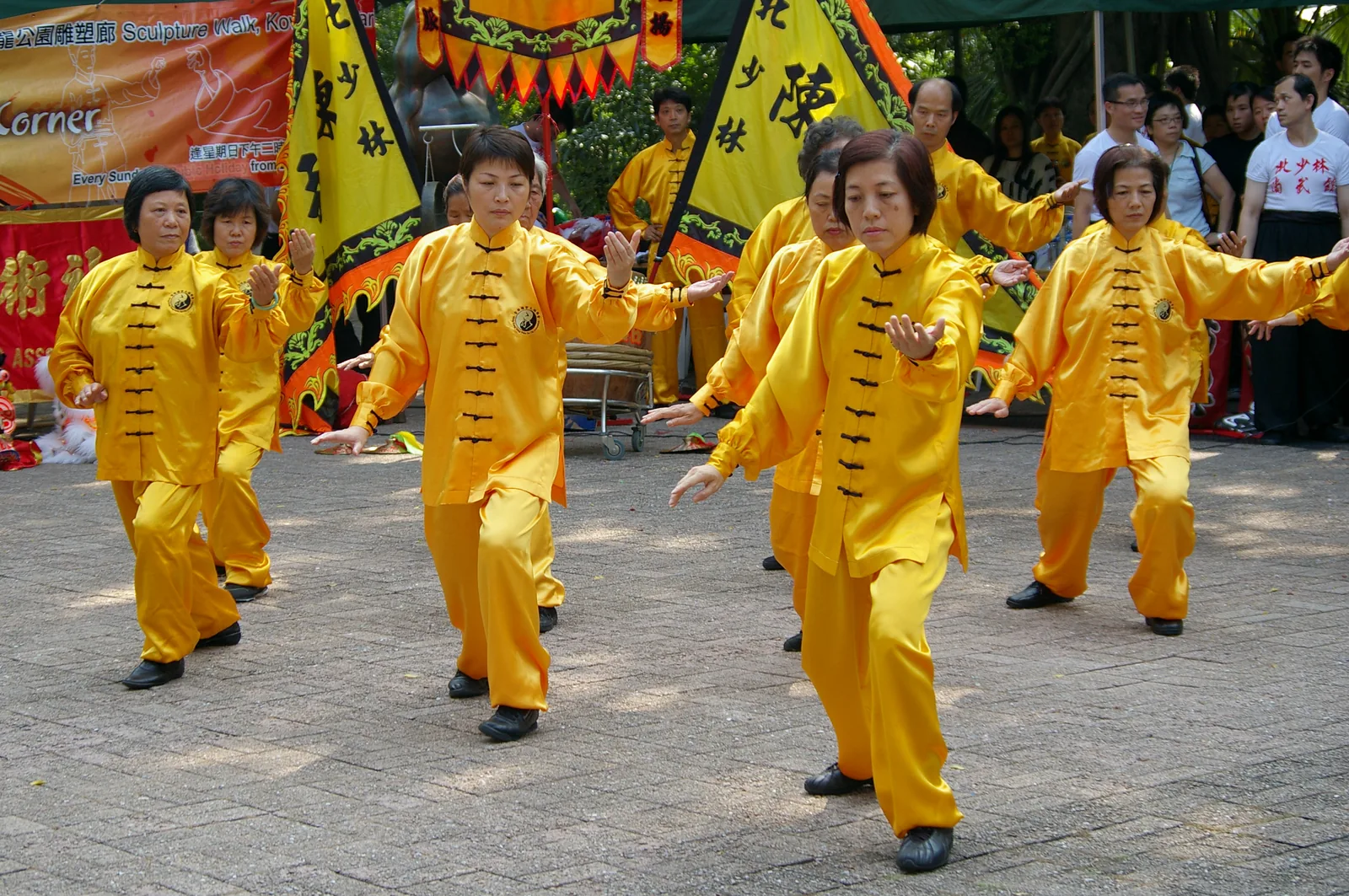 Group of Taijiquan practitioners in matching yellow silk uniforms performing synchronized forms at Kung Fu Corner in Kowloon Park, Hong Kong — UNESCO's 2020 inscription (File 00424) covers the Chen-style Taijiquan tradition originating in Chenjiagou, Henan, practiced by an estimated 300 to 400 million people worldwide