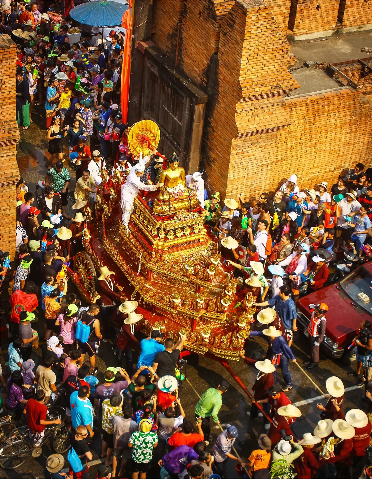 Aerial view of the Songkran festival golden Buddha statue procession at Chiang Mai's historic city wall surrounded by thousands of participants — UNESCO inscribed Songkran (File 01719, 2023) as a complete New Year ritual system including merit-making, almsgiving, Buddha image bathing, and water-pouring on elders' hands