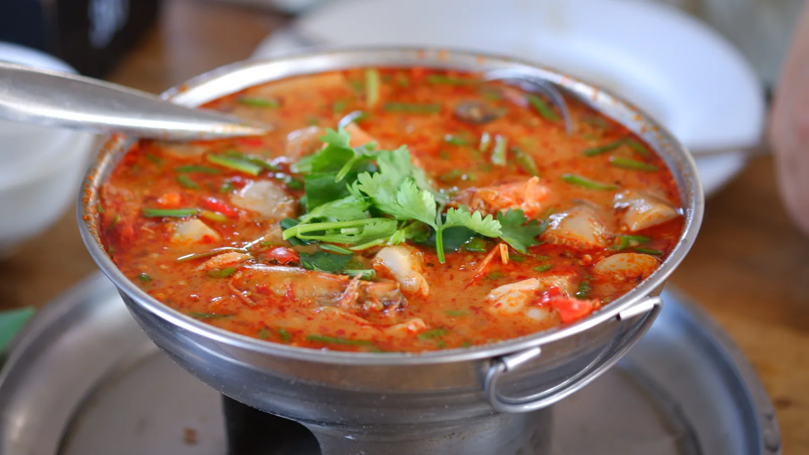 Tom Yum Kung hot and sour shrimp soup in a traditional Thai stainless steel pot with galangal, mushrooms, shrimp and cilantro garnish — UNESCO's 2024 inscription (File 01879) covers the ecological knowledge of aromatic herbs and the community practices of preparation, making it one of very few specific culinary preparations on the Representative List